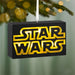 Star Wars logo ornament hanging on a Christmas tree with blurred lights in the background