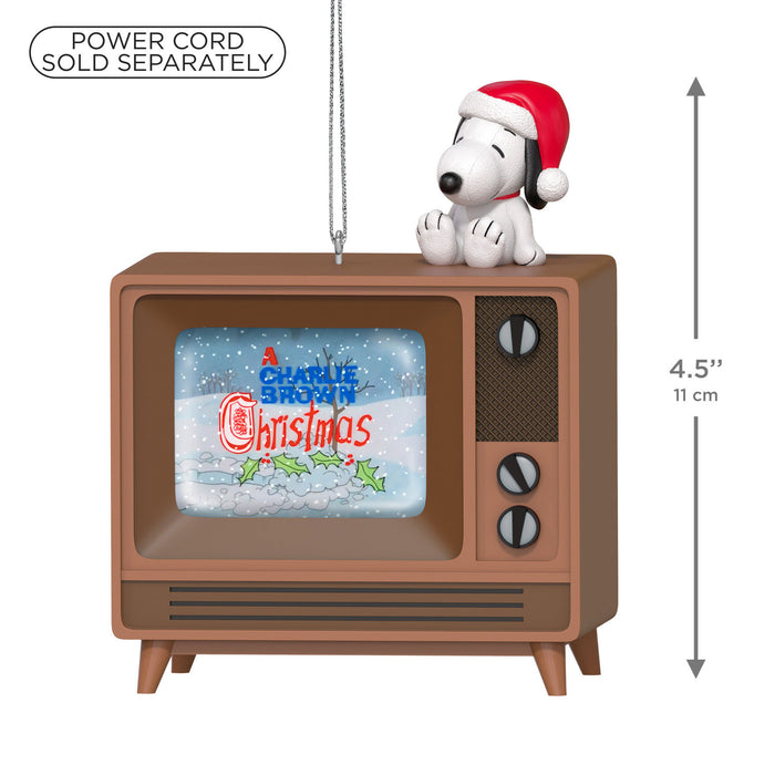 Decorative ornament of a dog in a Santa hat on an old-fashioned TV with 'A Charlie Brown Christmas' on screen, with text indicating power cord sold separately.