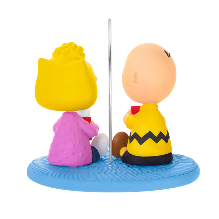 Two cartoon characters, one in yellow and pink and the other in yellow with a black zigzag pattern, sitting under an umbrella on a blue base.