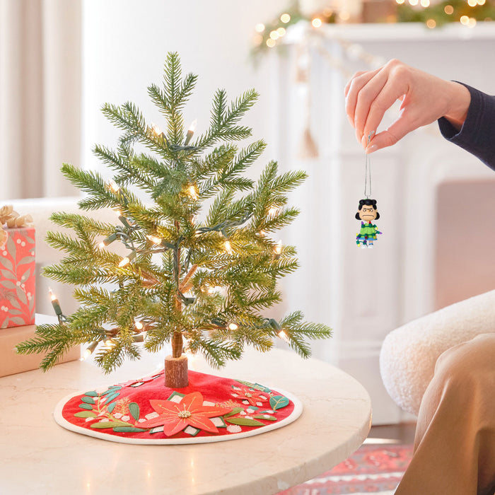 Person decorating a small Christmas tree with a figurine in a cozy living room.
