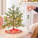 Person decorating a small Christmas tree with a figurine in a cozy living room.