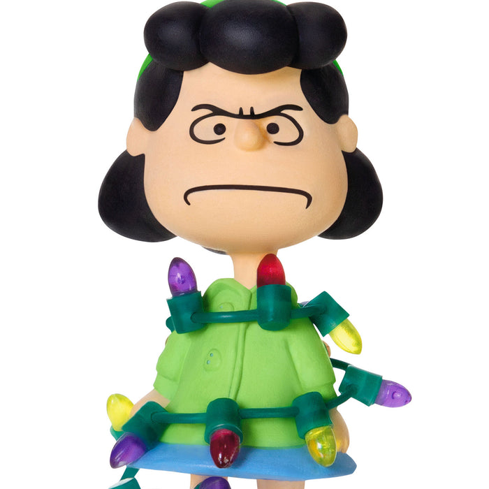 Toy figure of a character with black hair and green dress wrapped in Christmas lights on a white background