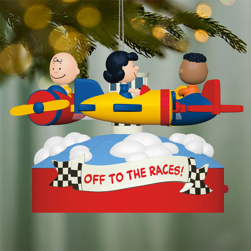 Decorative Christmas ornament with  three characters on an airplane ride featuring a banner 'Off to the Races!' and checkered flags against a blurred Christmas tree background.