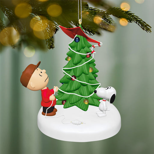 Christmas ornament with Charlie Brown and Snoopy decorating a tree against a blurred green background.