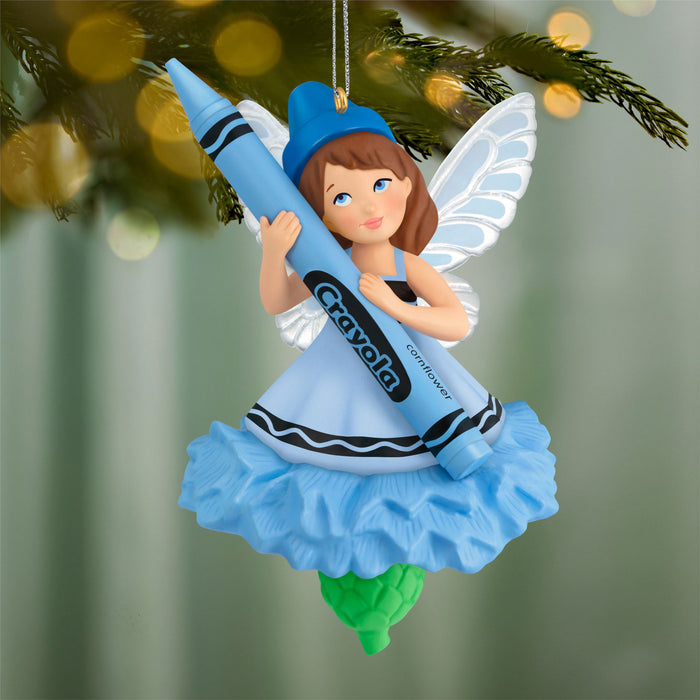 Crayon fairy ornament holding a blue Crayola crayon against a blurred Christmas tree background