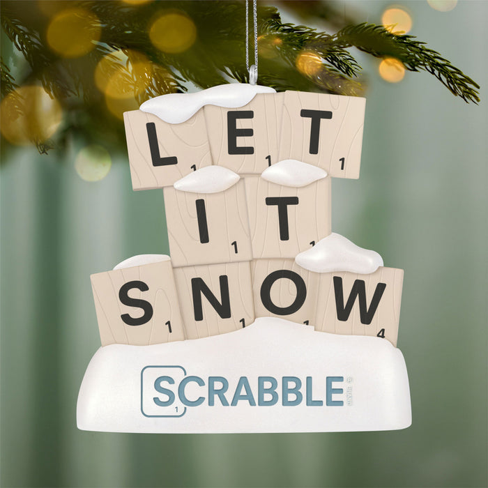 Scrabble tile ornament spelling 'LET IT SNOW' with a Scrabble logo, hanging on a Christmas tree.