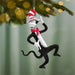 Ornament of Cat in the Hat hanging from a tree branch with blurred lights in the background.