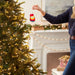 Person decorating a Christmas tree with a red tag in a festive living room.