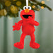 Elmo ornament hanging on a Christmas tree with blurred lights in the background