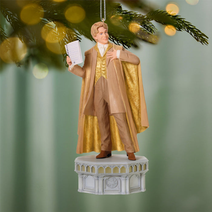 Decorative ornament of a man in a gold and brown outfit holding a book, hanging on a Christmas tree.
