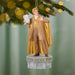 Decorative ornament of a man in a gold and brown outfit holding a book, hanging on a Christmas tree.