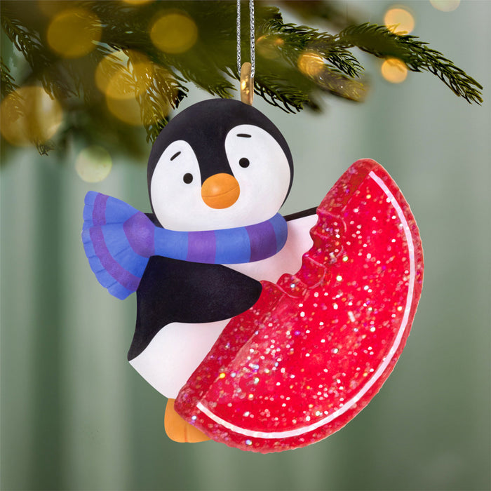 Penguin Christmas ornament with a red glittery disc on a blurred green background