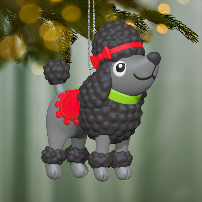 Decorative poodle ornament with a red bandana and green collar hanging on a Christmas tree.