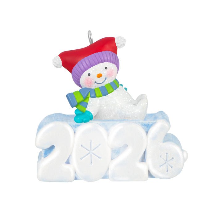 Decorative ornament with a snowman wearing a red hat and green scarf, sitting on the number '2026'.