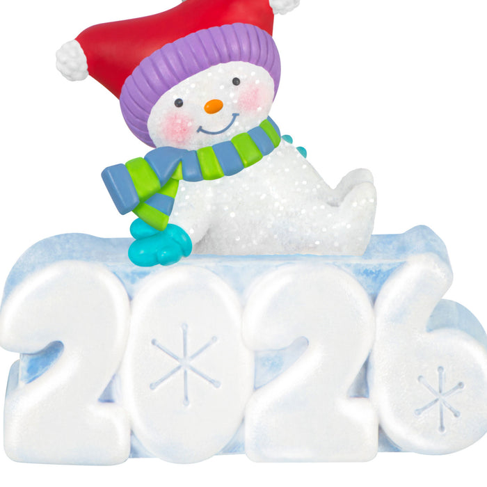 Snowman figurine with colorful hat and scarf on a '2026' block.