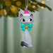 Cat-shaped Christmas ornament with a pink hat and green bow hanging on a tree.