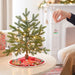 Person decorating a small Christmas tree with lights and ornaments in a cozy living room.
