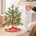 Person decorating a small Christmas tree with lights and ornaments in a cozy living room.