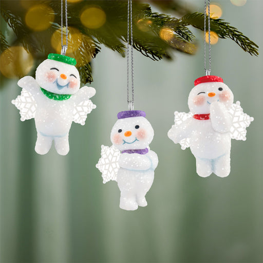 Three snowman ornaments with colorful hats hanging on a Christmas tree.