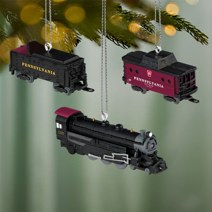 Three Pennsylvania Railroad train ornaments hanging on a Christmas tree.
