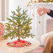 Small decorated Christmas tree on a table with a person hanging an ornament.