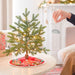 Small decorated Christmas tree on a table with a person hanging a ornament.