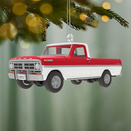 Red and white truck ornament hanging on a Christmas tree branch with blurred lights in the background.