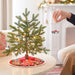 Small decorated Christmas tree on a table with a person hanging a ornament.