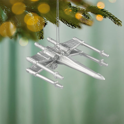 Silver spaceship ornament hanging on a Christmas tree with blurred lights in the background