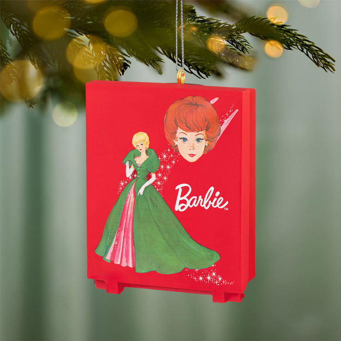 Barbie ornament with a red background featuring the Barbie character and logo, hanging on a Christmas tree.