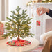 Small decorated Christmas tree on a table with a person hanging a red ornament.