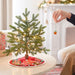 Small decorated Christmas tree on a table with a person's hand placing a ornament.