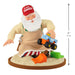 Toy figure of Santa Claus wearing a 'Claus Trucks' hat with a toy truck and tools on a white background.