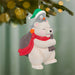 Decorative ornament of a polar bear and penguin hugging, wearing festive hats and scarves, against a blurred Christmas tree background.