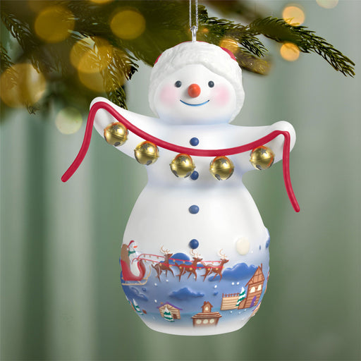 Decorative snowman ornament with jingle bells against a blurred Christmas tree background