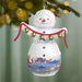Decorative snowman ornament with jingle bells against a blurred Christmas tree background