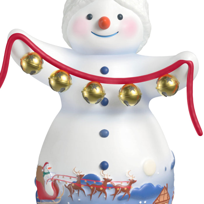 Decorative snowman figurine with gold bells and a Santa Claus scene on a white background
