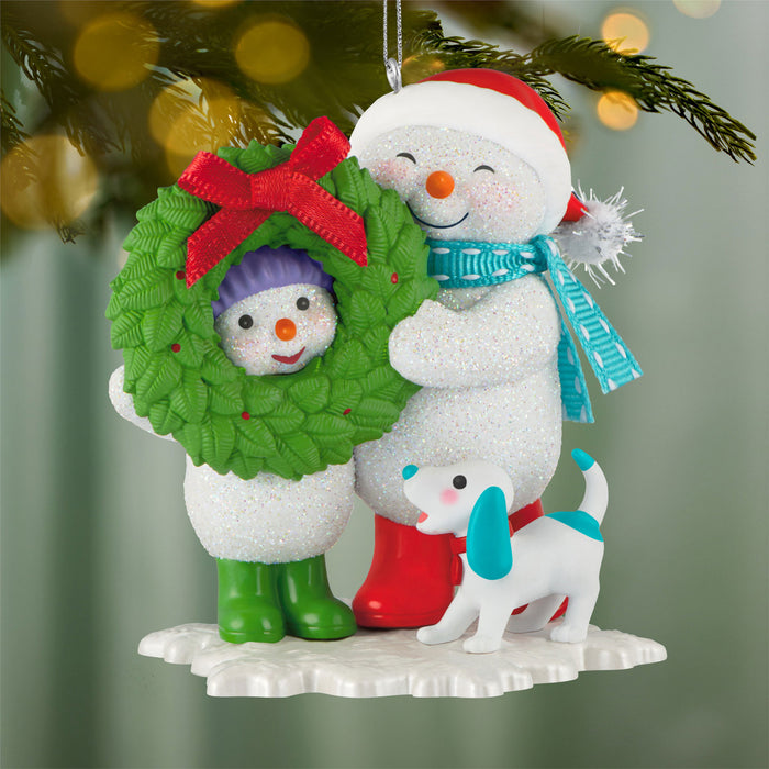 Christmas ornament featuring a snowman with a wreath, another snowman, and a dog on a green background.