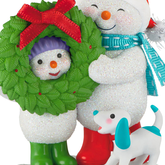 Two Christmas-themed figurines, one resembling a snowman in a wreath and the other with a dog, on a white background.