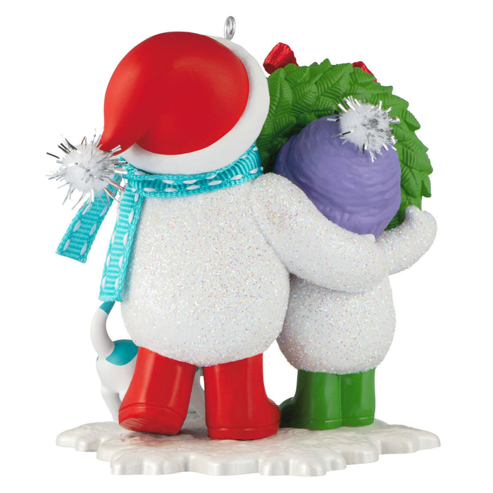 Decorative ornament of a snowman with a red hat, green scarf, and purple ball on a white background