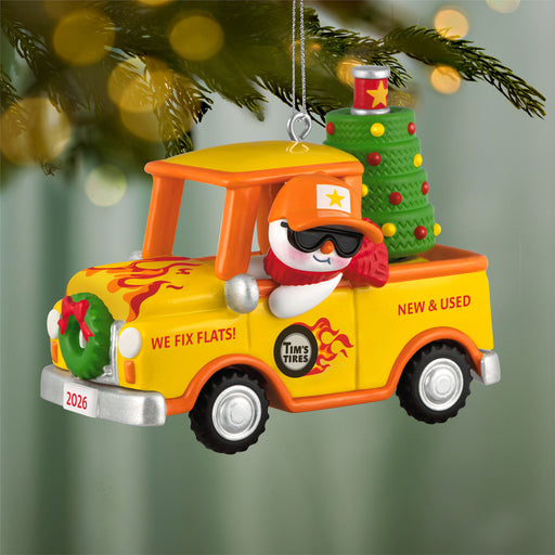 Christmas ornament of a yellow truck with a snowman driver, decorated with festive items, hanging on a tree.