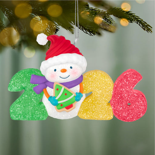 Decorative ornament with a snowman and numbers '2026' hanging on a Christmas tree.