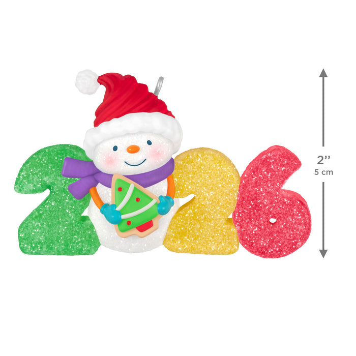 Decorative ornament with a snowman holding a Christmas tree and colorful numbers '2026'.