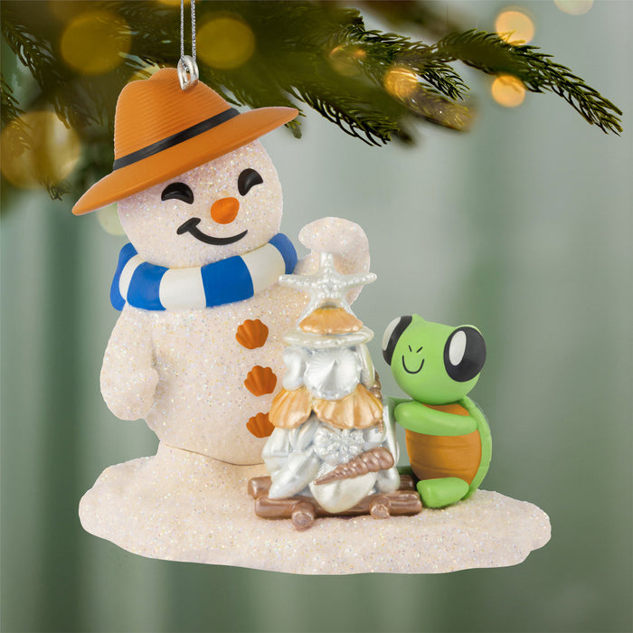 Decorative Christmas ornament with a snowman, turtle, and seashell stand on a blurred green background.