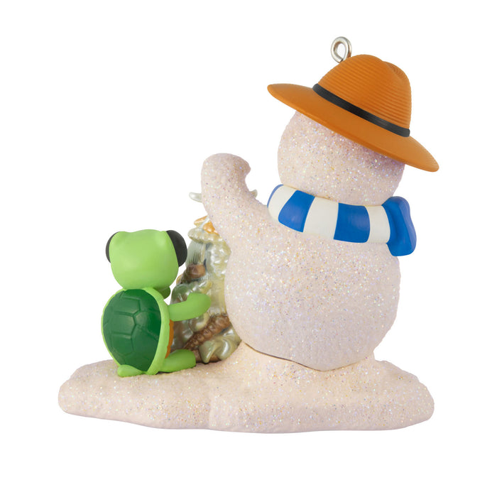 Decorative ornament of a snowman with a hat and scarf, holding a green turtle, on a white background.