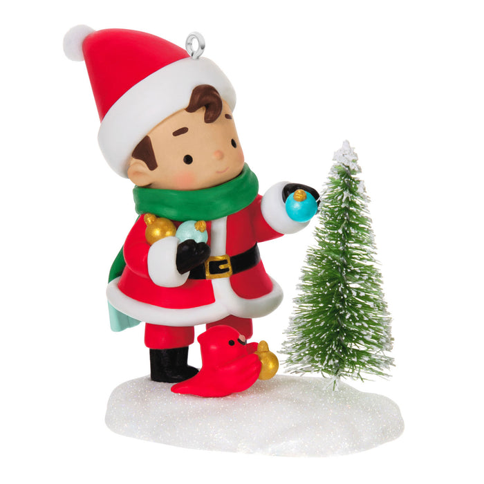 Christmas ornament of a child in Santa Claus outfit with a small tree and a little red feathered bird.