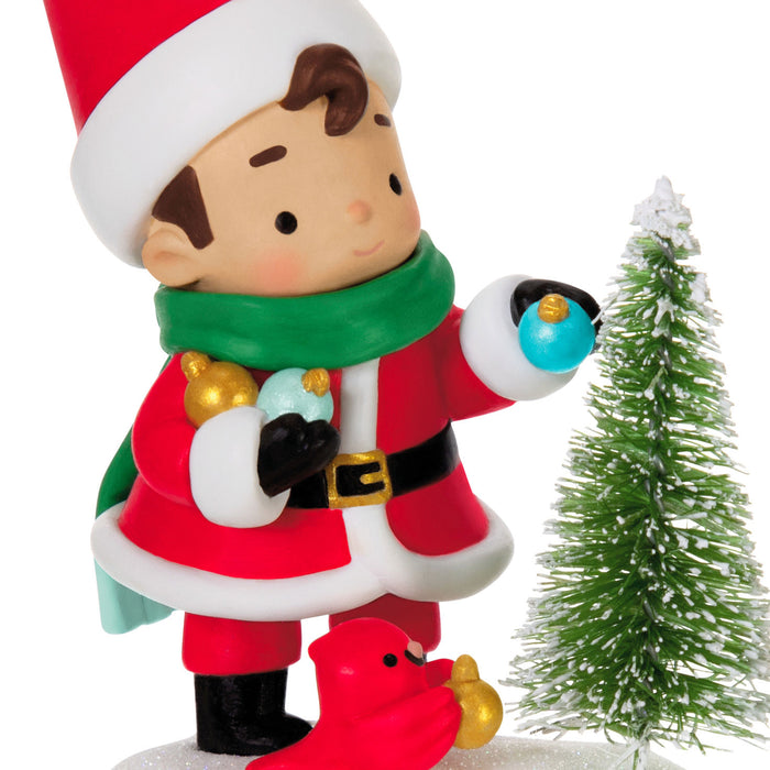 Christmas-themed figurine of a child in a Santa outfit with a small tree on a white background
