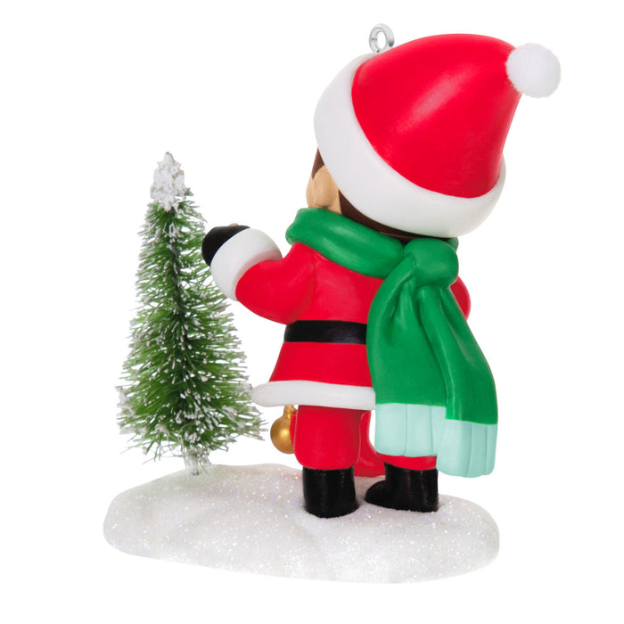 Christmas ornament of a person in Santa Claus outfit with a small tree on a white background