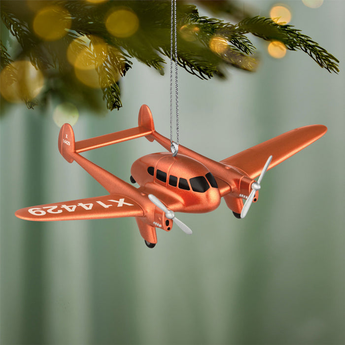 Orange airplane ornament hanging on a Christmas tree with a blurred green background