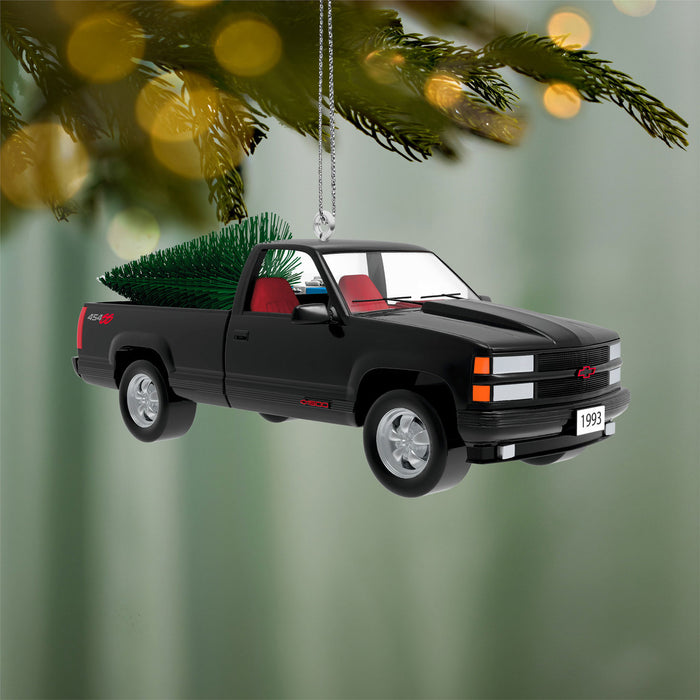 Black truck Christmas ornament with a tree in the bed, hanging from a tree.